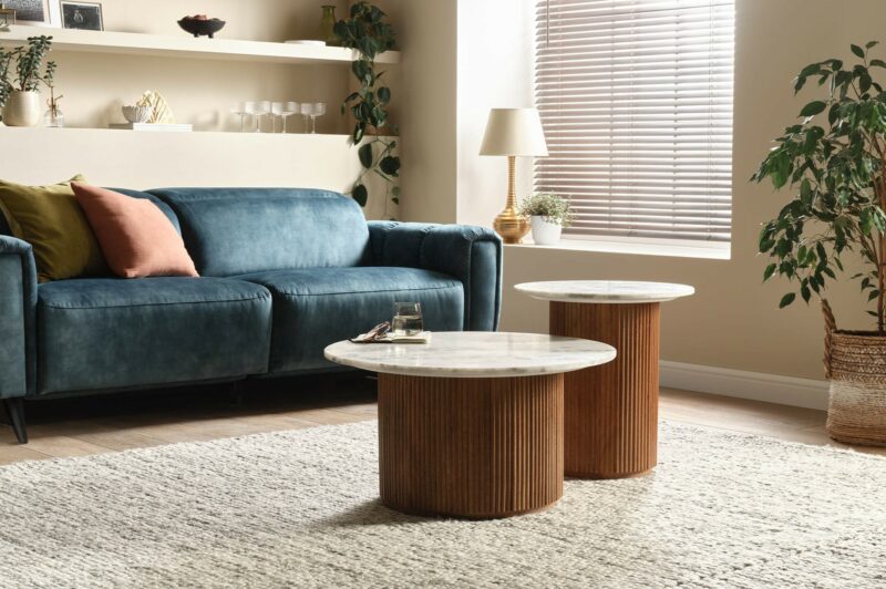 Oak Furnitureland fluted mango wood round coffee table and matching side table with solid marble tops, in a living room with a blue velvet sofa.