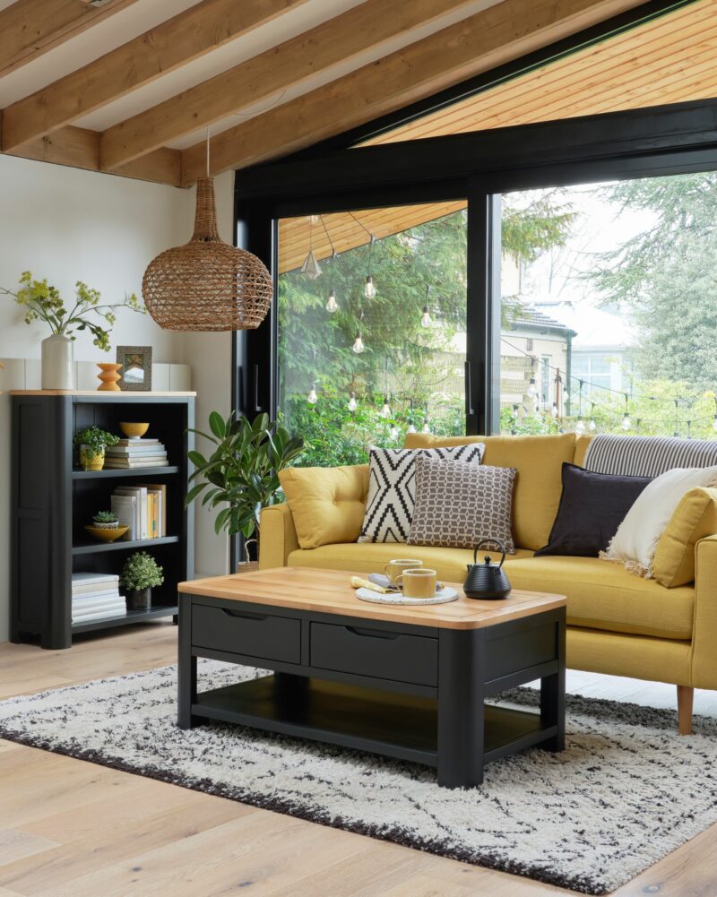 Oak Furnitureland dark grey painted Grove coffee table and small bookcase in bright living room with a yellow sofa.