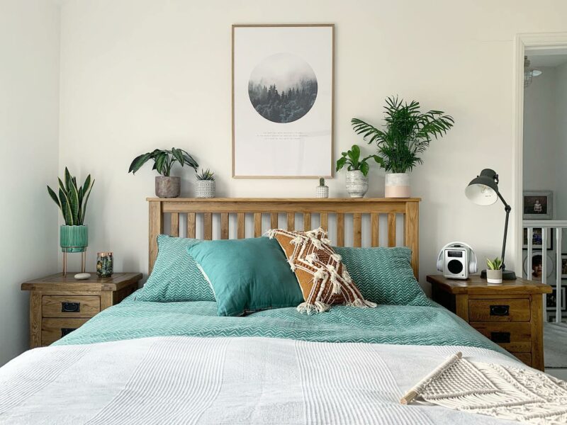 White bedroom with Original Rustic oak bedside tables and bed with teal bedding and decorated with lots of plants.