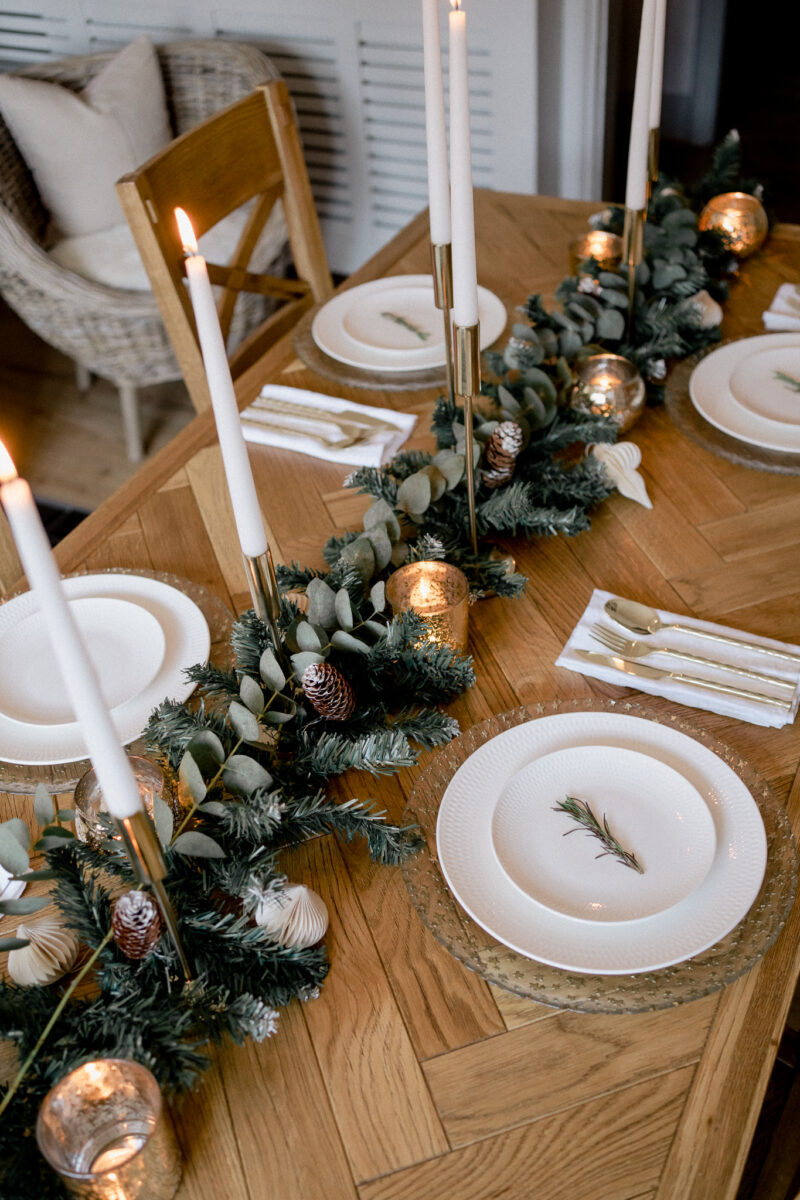 Parquet dning table set with a Christmas runner going down the middle, white taper candles and white crockery.
