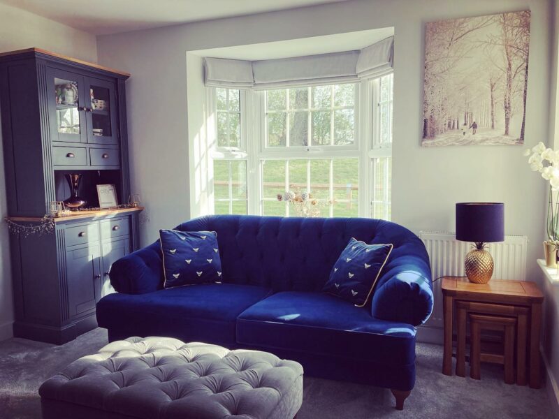 Living room with a blue painted Highgate dresser, navy velvet sofas and button back velvet footstool.