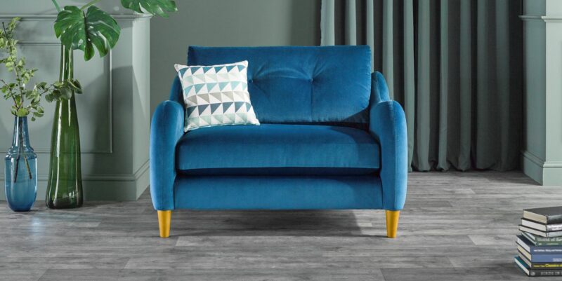 Vibrant blue Oak Furnitureland velvet Houston sofa styled next to houseplants and a stack of books.