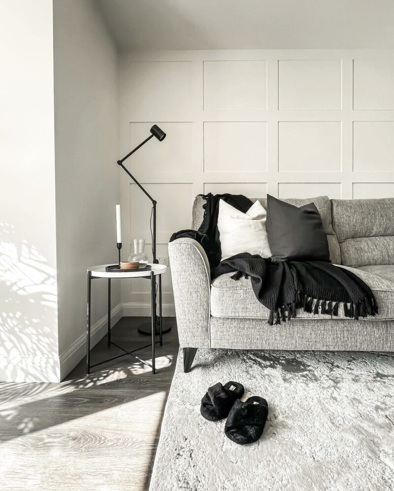 Grey Jenson sofa with black throw over arm. White and grey cushions. Black slippers on the floor. Modern decor
