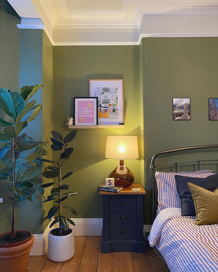 Olive green bedroom with plants, artwork and an inky blue painted bedside table.