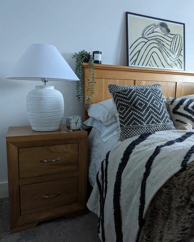 Oak Furnitureland natural oak Bevel bedside table next to bed with monochrome bedding and artwork displayed above
