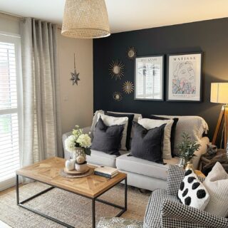 A sofa-living room furniture-beige sofa-houndstooth armchair-charcoal feature wall-monochrome cushions-wood and metal coffee table-wicker lampshade-floor standing lamp-jute rug-neutral linen curtain-wooden flooring-abstract wall art