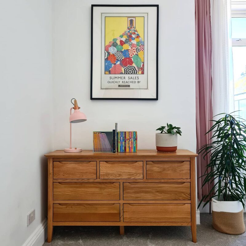 Copenhagen 7-drawer chest in a children's bedroom topped with a pink light, books and plants.