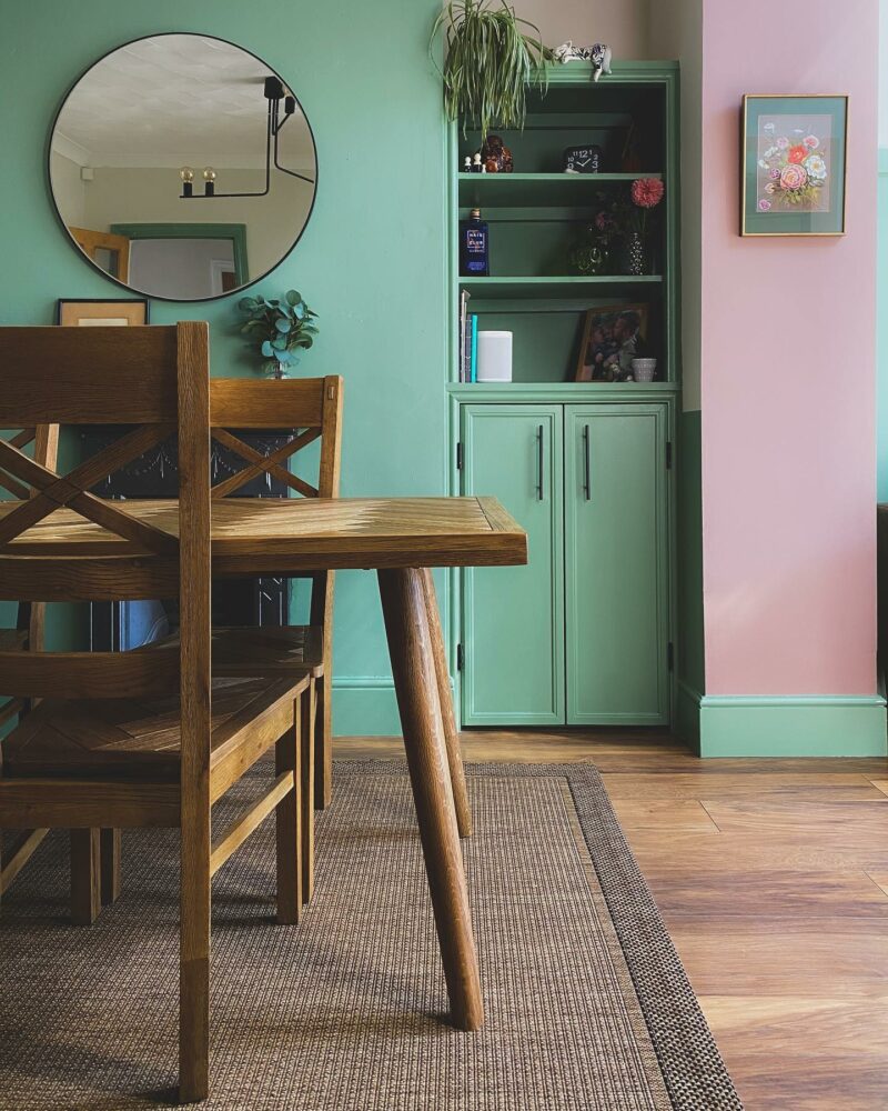 Parquet dining table in a vibrant green and pink period home, with in-built shelves styled with decorative accessories.