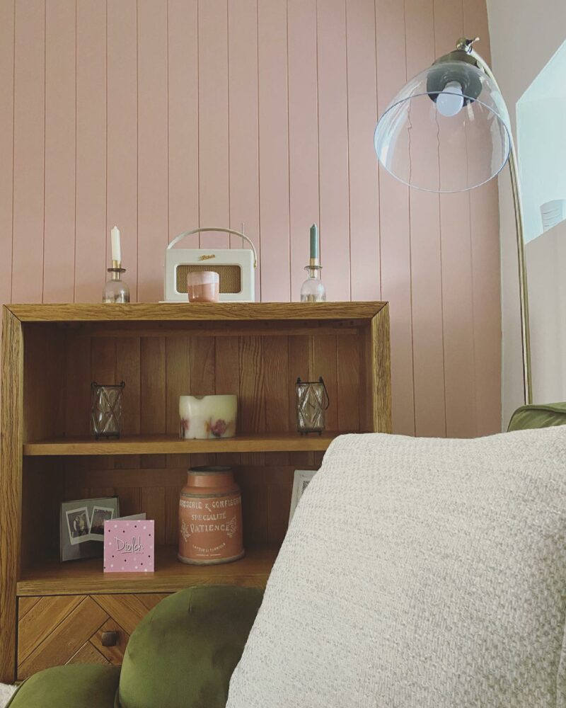 Parquet small oak bookcase next to a velvet olive green sofa in a pale pink living room.
