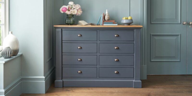 Oak Furnitureland inky blue Highgate 8-drawer chest in a bedroom with contrasting light blue walls.