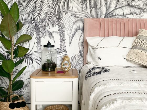 Oak Furnitureland white and oak Romsey bedside table with monochrome wallpaper, pink upholstered bed and plants.