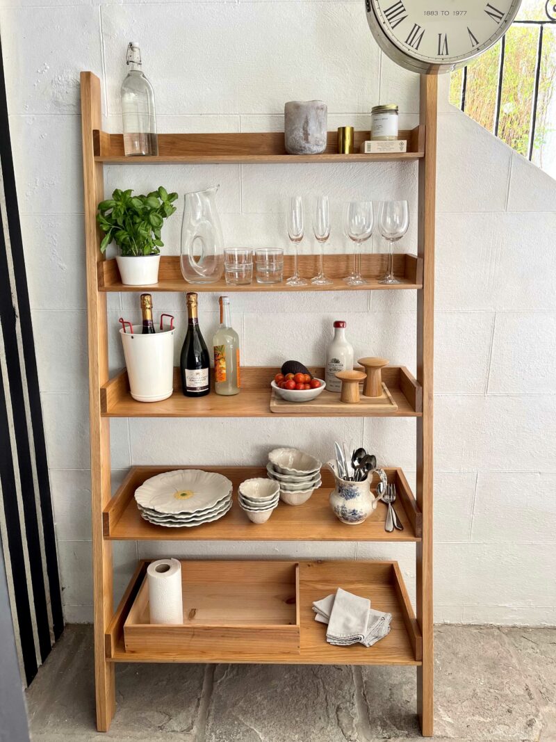 Natural oak open shelving unit filled with crockery, herbs, glassware and drinks.