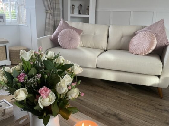Oak Furnitureland cream Evie sofa with pink accent cushion and cream and pink flowers and a candle in the forefront of the image.