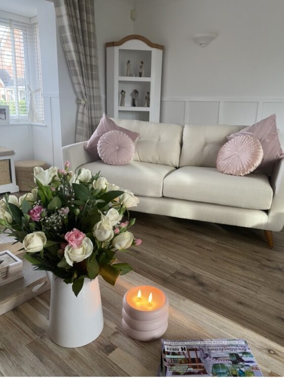 Oak Furnitureland cream Evie sofa with pink accent cushion and cream and pink flowers and a candle in the forefront of the image.