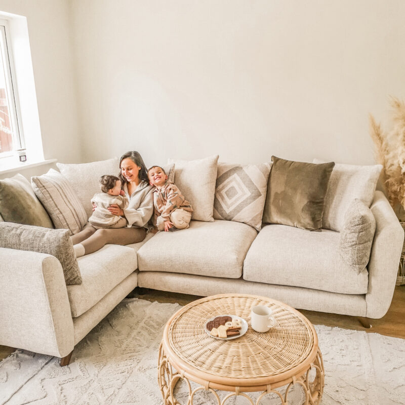 Oak Furnitureland Willoughby corner sofa in a neutral fabric with mum and baby sitting on in a living room.