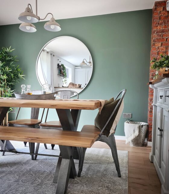 Oak and metal industrial-style Brooklyn dining table with green walls and plants.