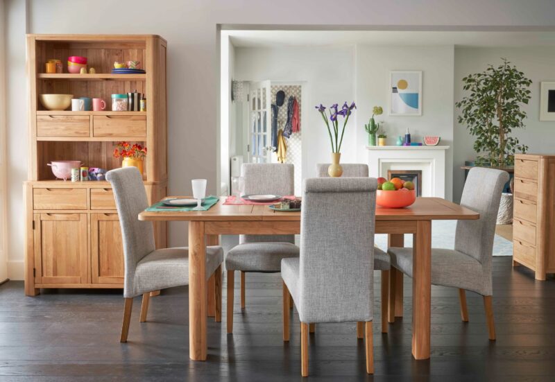 Romsey extendable natural oak dining table paired with grey upholstered chairs and decorated with bright accessories.