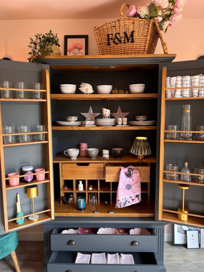 Oak Furnitureland Highgate blue larder pictured open and styled with pink accents.