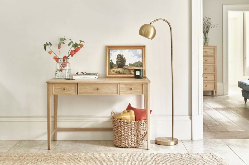 Neutral hallway with the Newton desk used as a console table, topped with a piece of art and flowers, with a gold floor lamp and a basket of cushions.