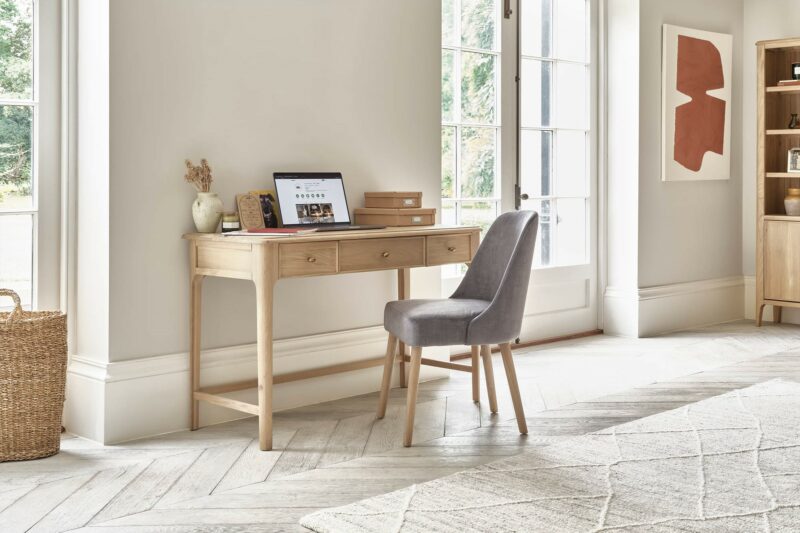 Newton natural oak desk in a large light-filled office space with a grey velvet chair.