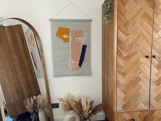 Parquet oak wardrobe in a bedroom with gold accessories, a textured wall hanging and house plants.