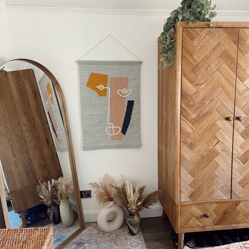 Parquet oak wardrobe in a bedroom with gold accessories, a textured wall hanging and house plants.