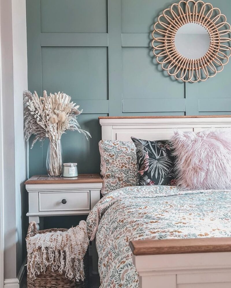 Matching pale grey painted bed and bedside table in a green panelled bedroom with floral bedding.