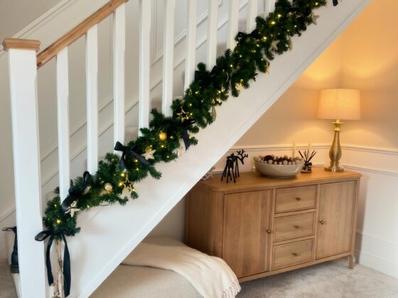 A staircase and sideboard-hallway furniture-natural oak large sideboard-hallway storage-neutral fabric footstool-beige carpet-white staircase-festive garland-brass table lamp