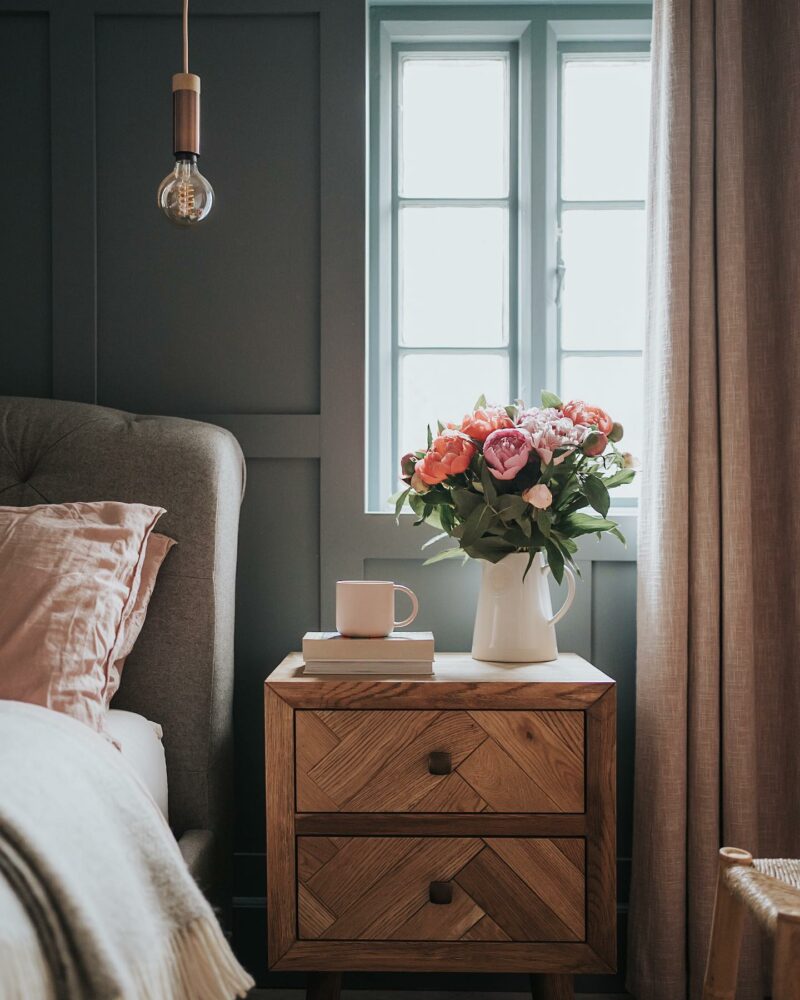 Oak Furnitureland Parquet bedside table in green panelled bedroom with a beautiful white jug filled with pink flowers.