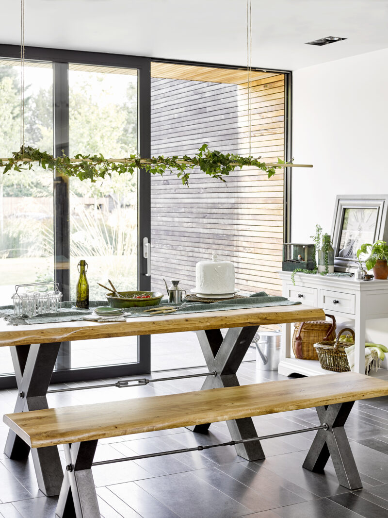Brooklyn dining table and benches in a light-filled dining room, styled with greenery and summery tableware. 