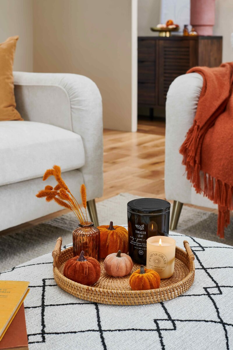 Close up of pumpkin decor on a pattern footstool, with cream sofas and orange throws and cushions.