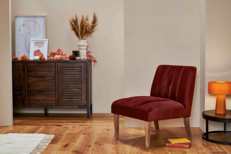 Burgundy velvet accent chair with oak legs in a room with a dark oak and metal sideboard and coffee table.