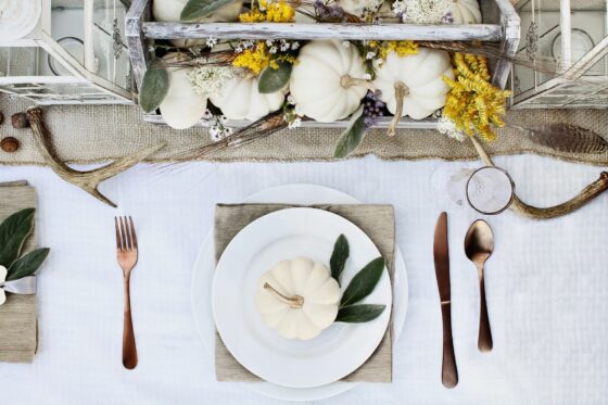 Table set for stylish Halloween meal with white tablecloth, white mini pumpkins and gold cutlery.