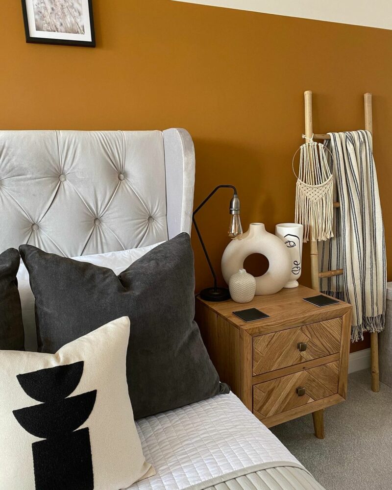 Mustard walls with grey velvet upholstered bed and neutral accessories.