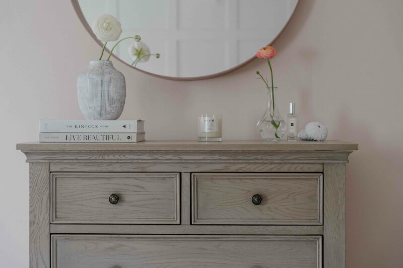 Front on shot of Oak Furnitureland Burleigh weathered oak chest of drawers styled with decorative accessories and a mirror hanging above.