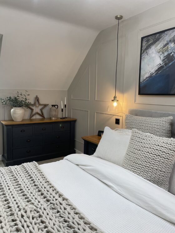 Bedroom with a close up of a chunky throw, with a blue painted chest of drawers with an oak top and soft accent lighting.