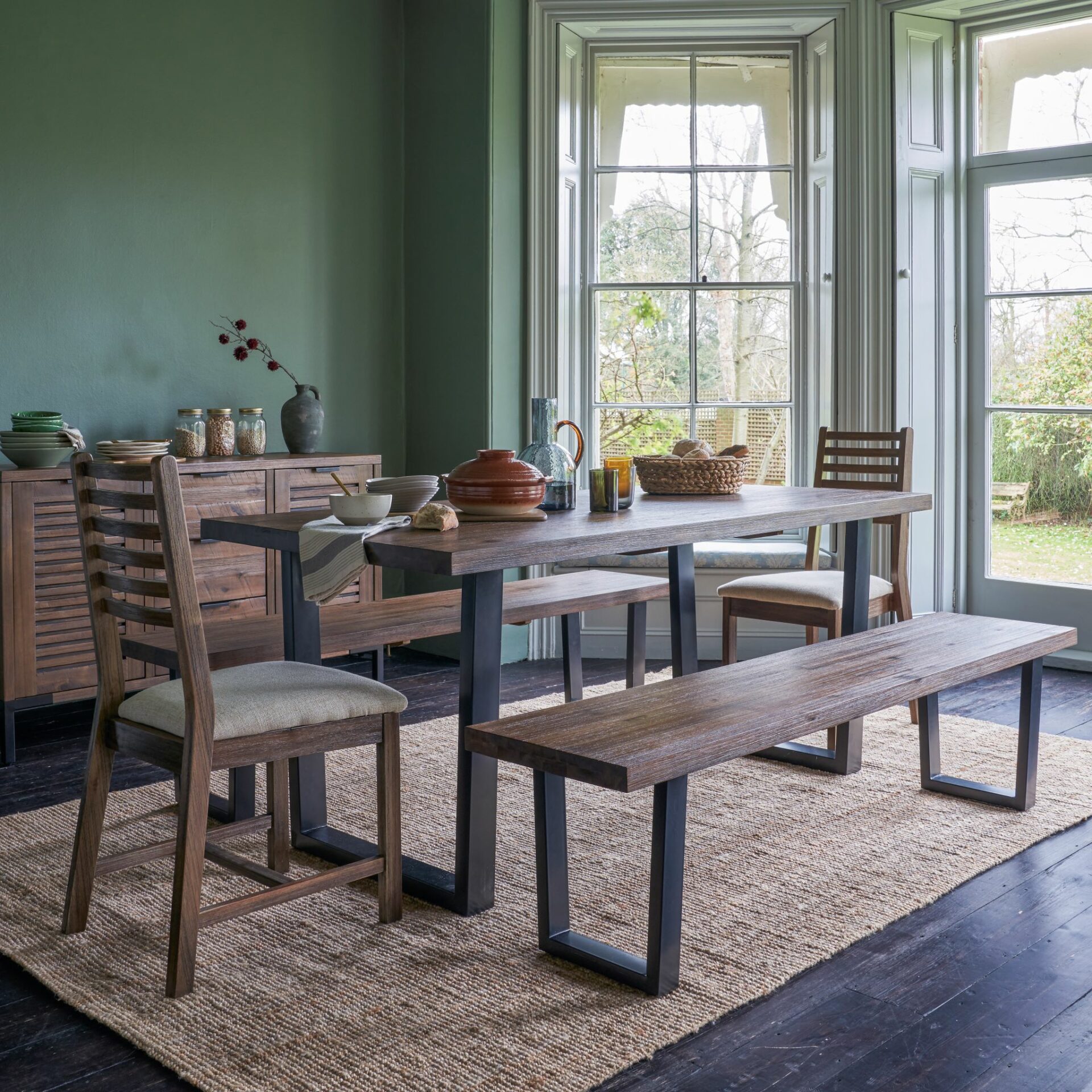 Detroit dark hardwood dining table with chairs and bench in light and airy dining room with green walls.
