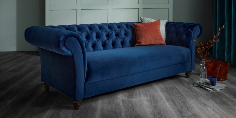 Oak Furnitureland navy velvet Montgomery Chesterfield-style sofa, wtih burnt orange and patterned scatter cushion.
