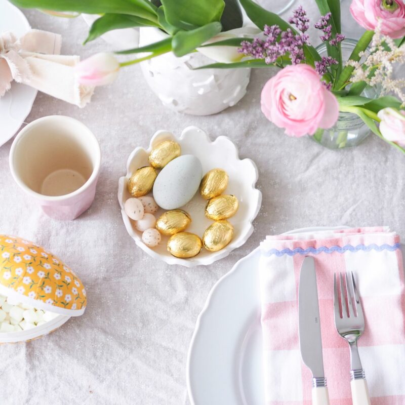 Easter table flat lay with delicate spring flowers, mini gold Easter eggs and gingham napkins.