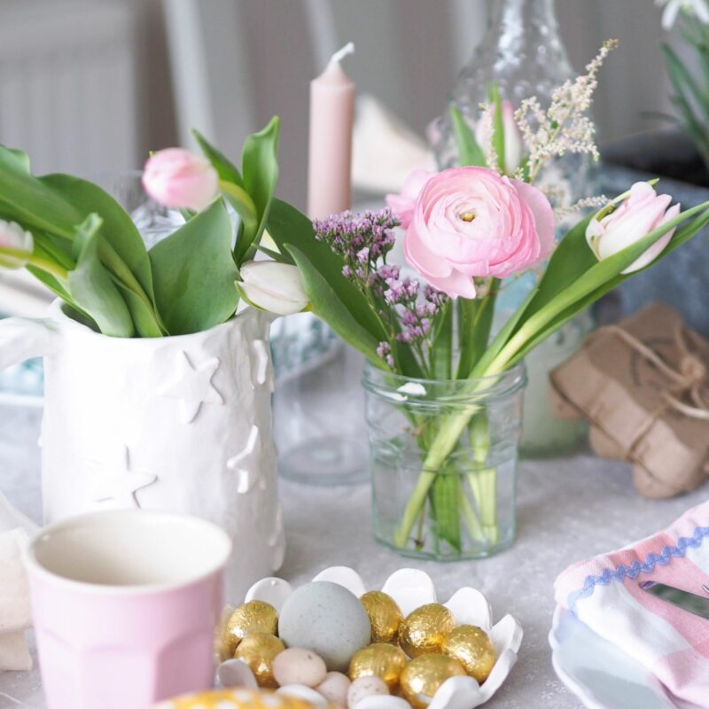 Easter tablescape with tulips and ranunculus in a jam jar, gold mini Easter eggs and pastel napkins.