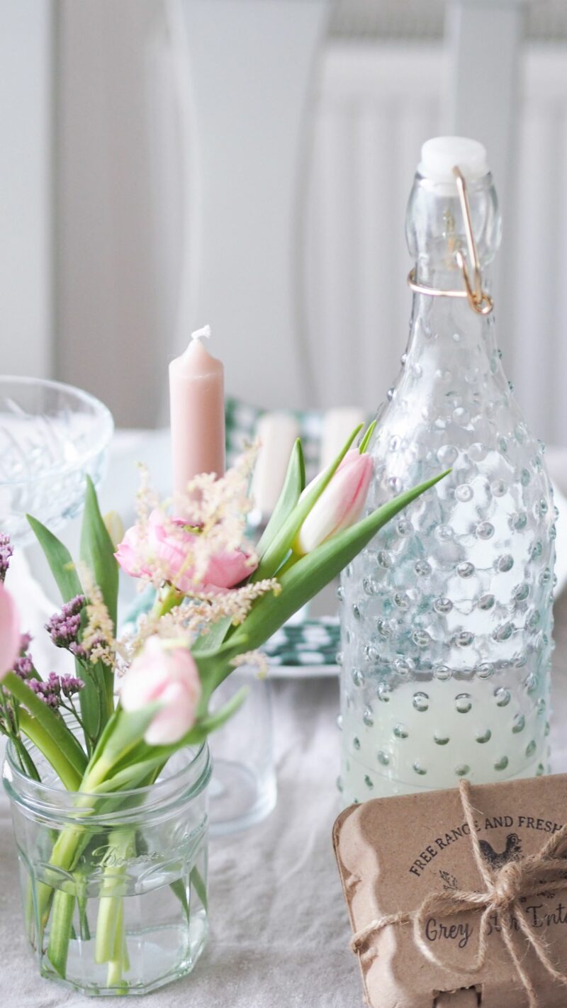 Spring table decorated with pastel flowers in a jam jar, pale pink candles and glassware.