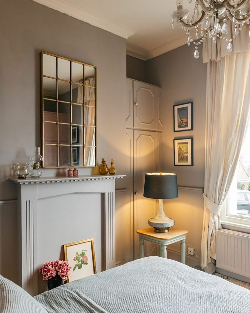 Elegant grey bedroom in a period home with a gold mirror, accent lighting from a lamp and decorative details.