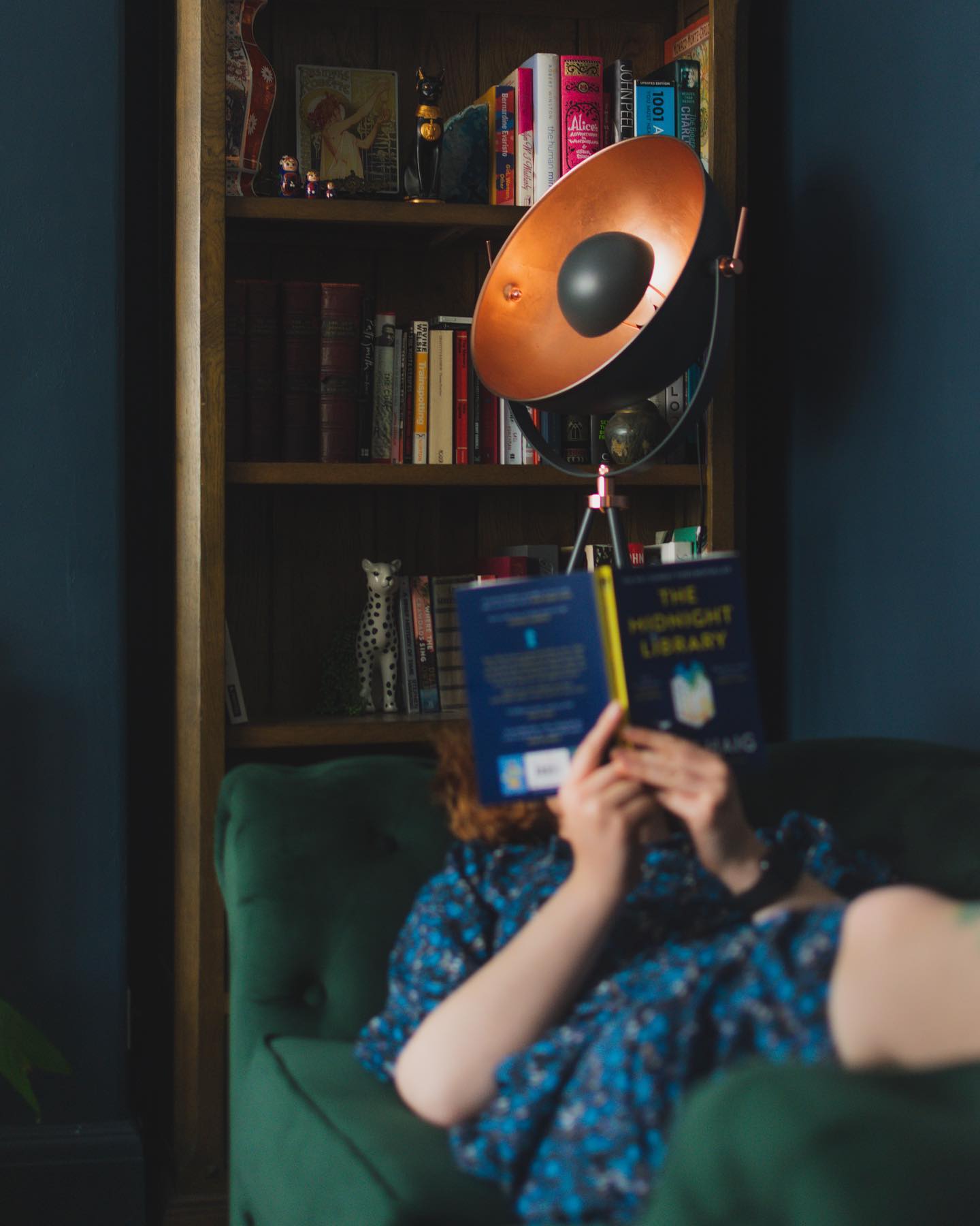Oak Furnitureland oak bookcase featured in the background behind a woman lying on a green sofa reading a book.