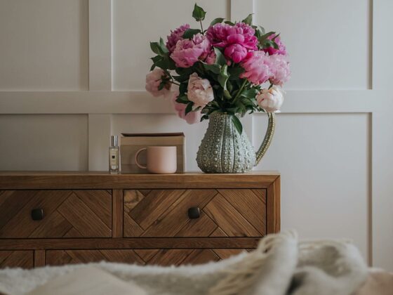 Parquet chest of drawers in a cream bedroom with a jug of pink flowers on top.
