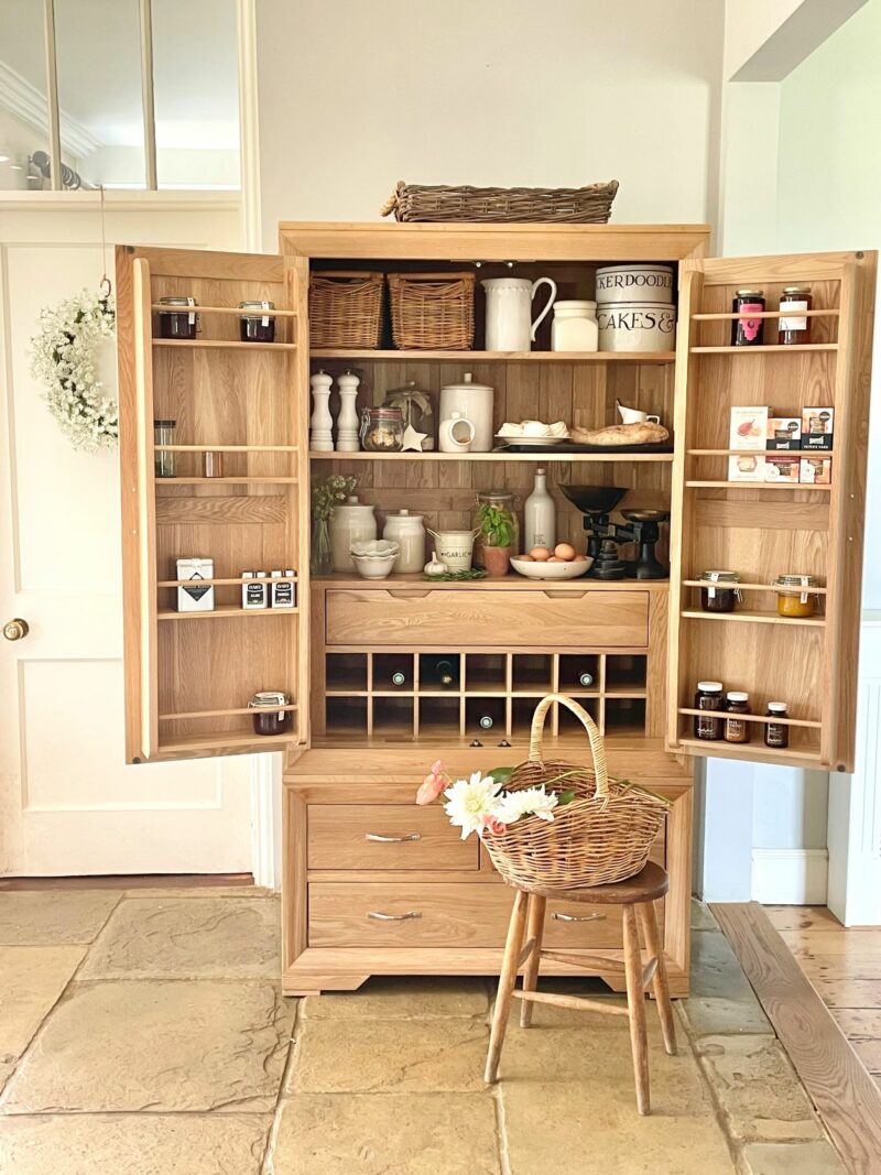 Natural oak Bevel larder open filled with wine, kitchen accessories and crockery.