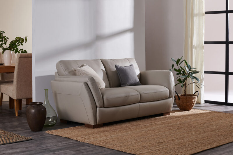 Neutral leather sofa in a living room with hessian rug and plants.