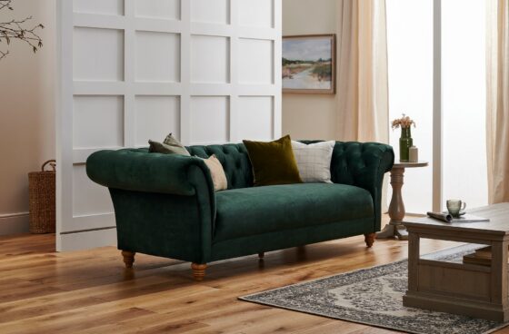 Green velvet Montgomery Chesterfield-style sofa in a room with weathered oak furniture and a patterned rug.