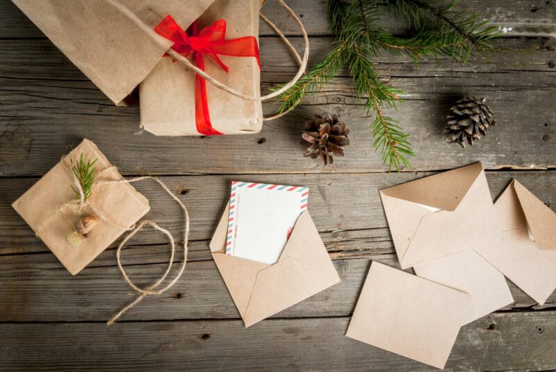 Brown paper wrapping and recycled Christmas cards surrounded by pinecones and greenery.