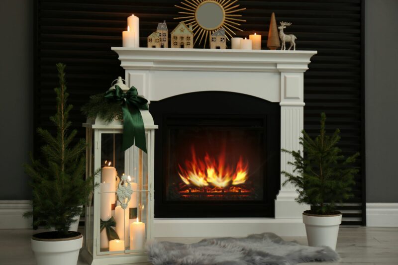 Potted Christmas trees next to a roaring fire surrounded by Christmas ornaments and decorations.