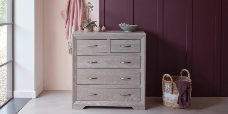 Grey wash 5-drawer unit in a room with pink and purple walls and decorative accessories and basket.